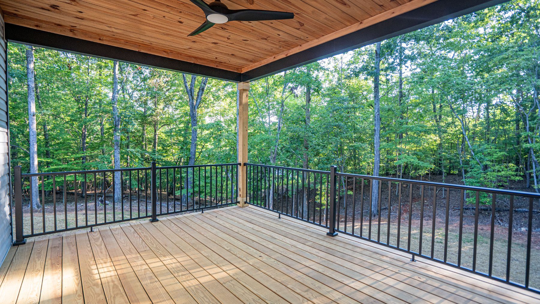 Covered back deck with a wood ceiling and ceiling fan overlooking the woods at Raven's Ridge
