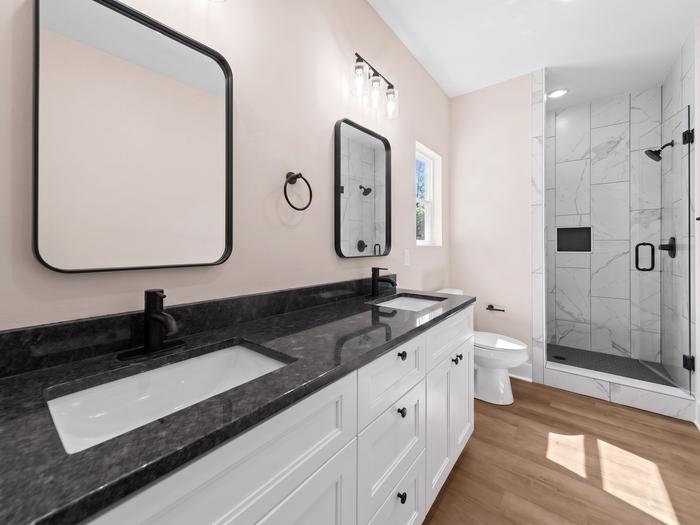 Double vanity with a granite countertop and tiled walk-in shower